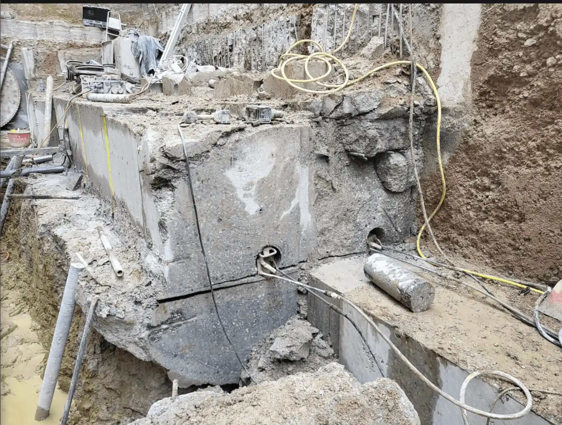 Betonsäge schneidet Fundament im Aushub, Kernbohrung und Schläuche sichtbar