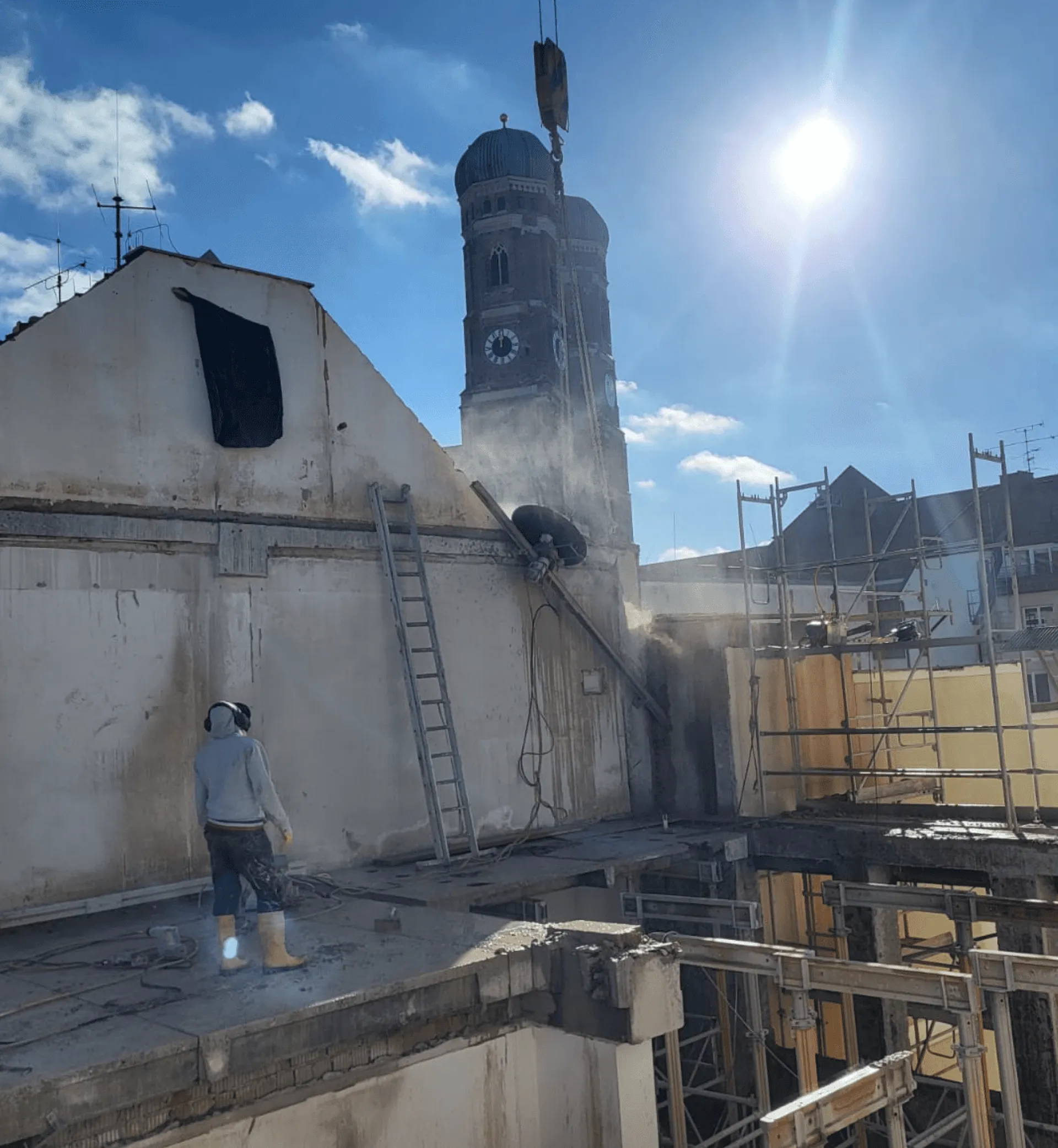 Betonsanierung auf Baustelle mit Staub, Gerüst und Kirchturm im Hintergrund
